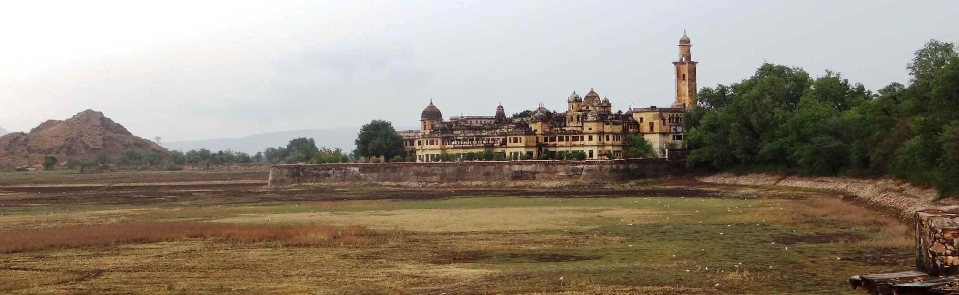 Wide panoramic landscape of the historic yellow stone Vijay Mandir Palace with its grand domes and watchtower, fronted by the grassy dry bed of Vijay Sagar Lake in Alwar, Rajasthan, serving as a vintage cinematic shooting location. film shooting locations in Banda, video shooting locations in Banda, tv shooting locations in Banda, shooting locations in Banda