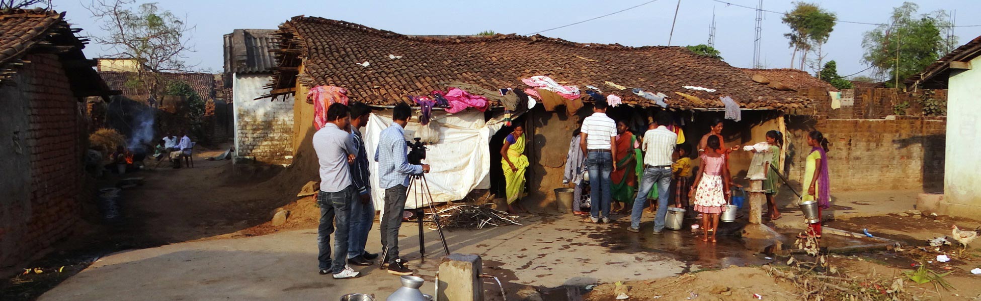 A professional video production crew filming a social impact documentary on location in a rural village in Bhawanipatna, Kalahandi, Odisha, showing filmmakers with a camera tripod interacting with local residents. fixer in Banda, film fixer in Banda, media fixer in Banda, movie fixer in Banda, production fixer in Banda, line producer in Banda
