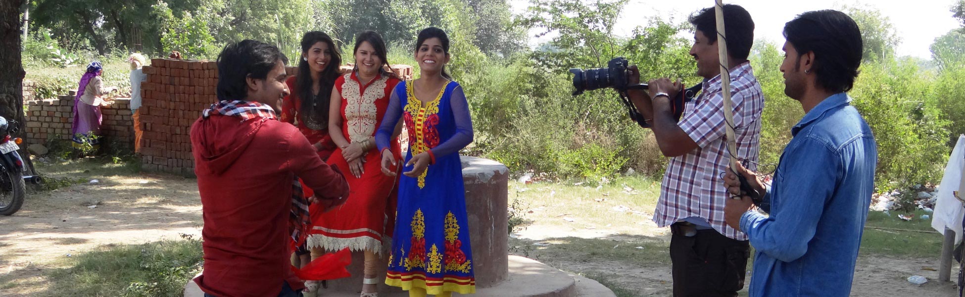 Behind-the-scenes view of an Indian short film production titled 'Don't Harass the Girl' in Ghaziabad, Uttar Pradesh. A videographer captures a scene featuring actors outdoors, including a man on a motorcycle looking toward a group of women in traditional attire. film production house in bangladesh, film production house in dhaka, video production house in bangladesh, video production house in dhaka, tv production house in bangladesh, tv production house in dhaka, production house in bangladesh, production house in dhaka, film production company in bangladesh, film production company in dhaka, video production company in bangladesh, video production company in dhaka, tv production company in bangladesh, tv production company in dhaka, production company in bangladesh, production company in dhaka