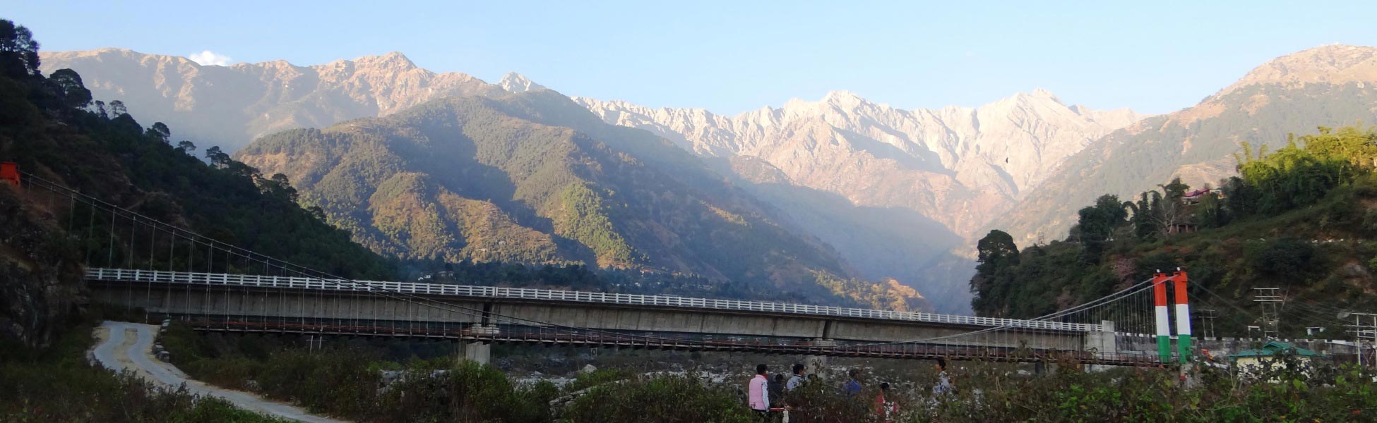 A wide panoramic view of the rugged Dhauladhar mountain range rising behind a long concrete and suspension bridge at Saurabh Van Vihar in Palampur, Himachal Pradesh, India. fixer in Banka, film fixer in Banka, media fixer in Banka, movie fixer in Banka, production fixer in Banka, line producer in Banka