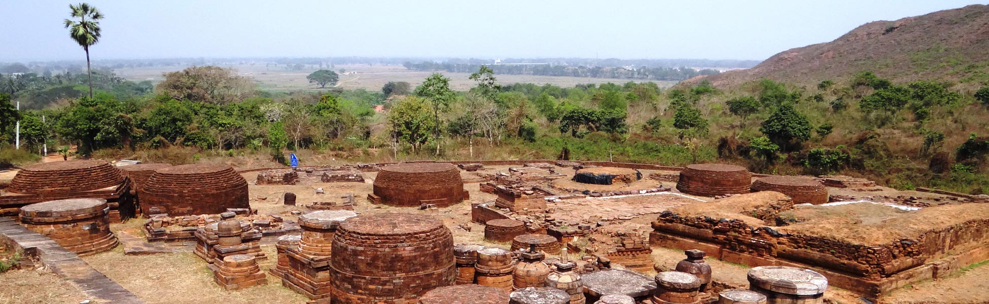 Panoramic view of the ancient red brick stupas and monastic ruins at the Lalitgiri Buddhist complex in Odisha, India, surrounded by lush green hills. fixer in Banswara, film fixer in Banswara, media fixer in Banswara, movie fixer in Banswara, production fixer in Banswara, line producer in Banswara