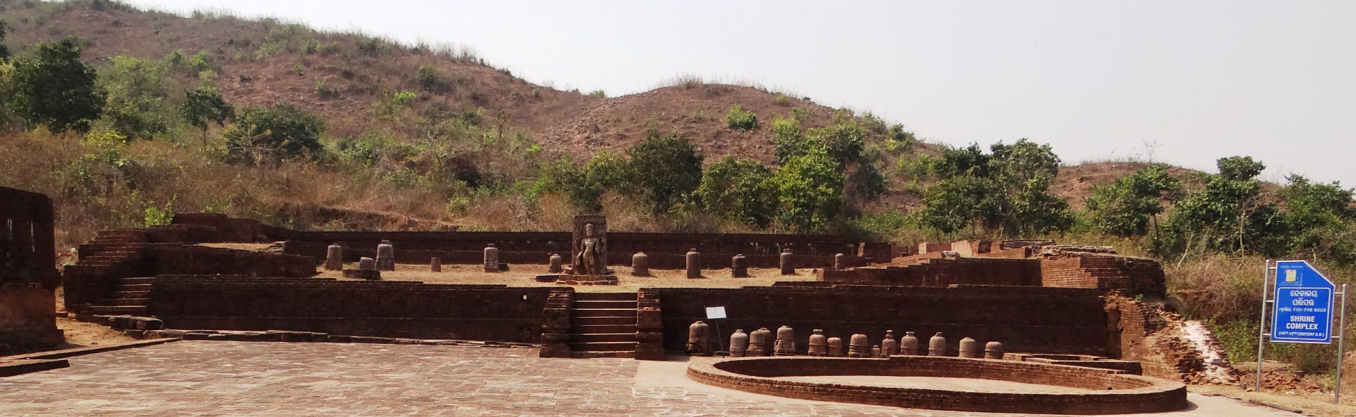Excavated 10th to 12th-century brick shrine complex at Udayagiri Buddhist site in Jajpur, Odisha, India, featuring a central stone deity sculpture, multiple stone votive stupas on a terraced platform, and a hillside backdrop. fixer in Barabanki, film fixer in Barabanki, media fixer in Barabanki, movie fixer in Barabanki, production fixer in Barabanki, line producer in Barabanki