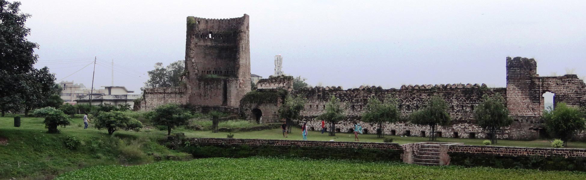 The ancient red-brick fortification wall and rectangular defensive watchtower of Nurpur Fort in Kangra, Himachal Pradesh, with stone paths overlooking a sunken dry moat area. film production house in Basirhat, video production house in Basirhat, tv production house in Basirhat, production house in Basirhat, film production company in Basirhat, video production company in Basirhat, tv production company in Basirhat, production company in Basirhat