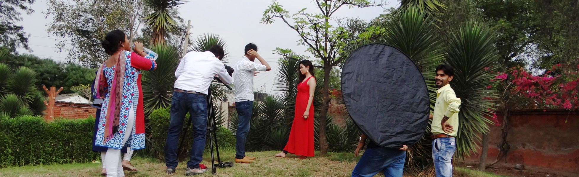 Behind-the-scenes of a music video production in Delhi by Trisna Films, showing a camera operator with a tripod, director coordinating, and an actress in a red dress during an outdoor shoot with lighting reflectors. film shooting locations in Basirhat, video shooting locations in Basirhat, tv shooting locations in Basirhat, shooting locations in Basirhat