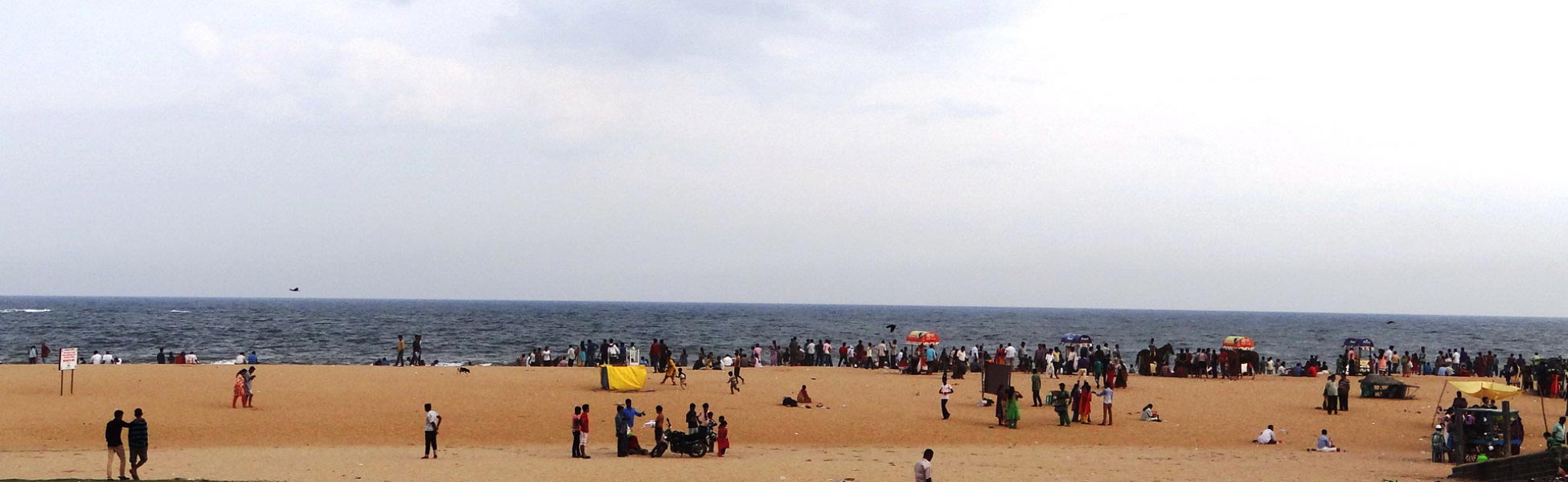 Wide panoramic view of the sandy shoreline at Marina Beach in Chennai, featuring local crowds, small beach stalls, and the ocean under an open sky; an active location scout reference for line production and film crowd management in Tamil Nadu. fixer in Basti, film fixer in Basti, media fixer in Basti, movie fixer in Basti, production fixer in Basti, line producer in Basti
