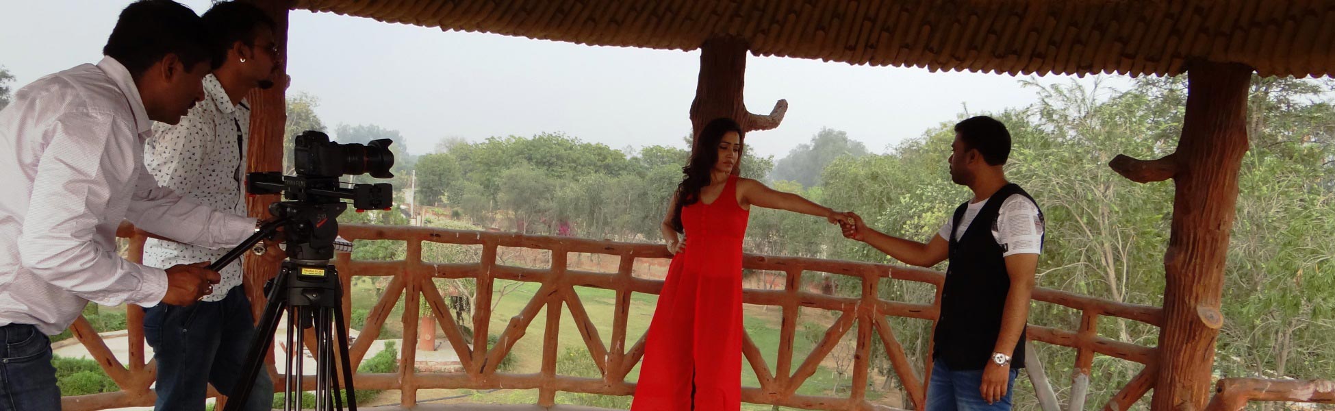 Trisna Films camera crew setting up a professional cinema camera on a tripod to shoot a romantic scene featuring an actress in a red dress and an actor under a wooden pavilion for the 'Humsafar Ki Talash Mein' music video production. fixer in Begusarai, film fixer in Begusarai, media fixer in Begusarai, movie fixer in Begusarai, production fixer in Begusarai, line producer in Begusarai