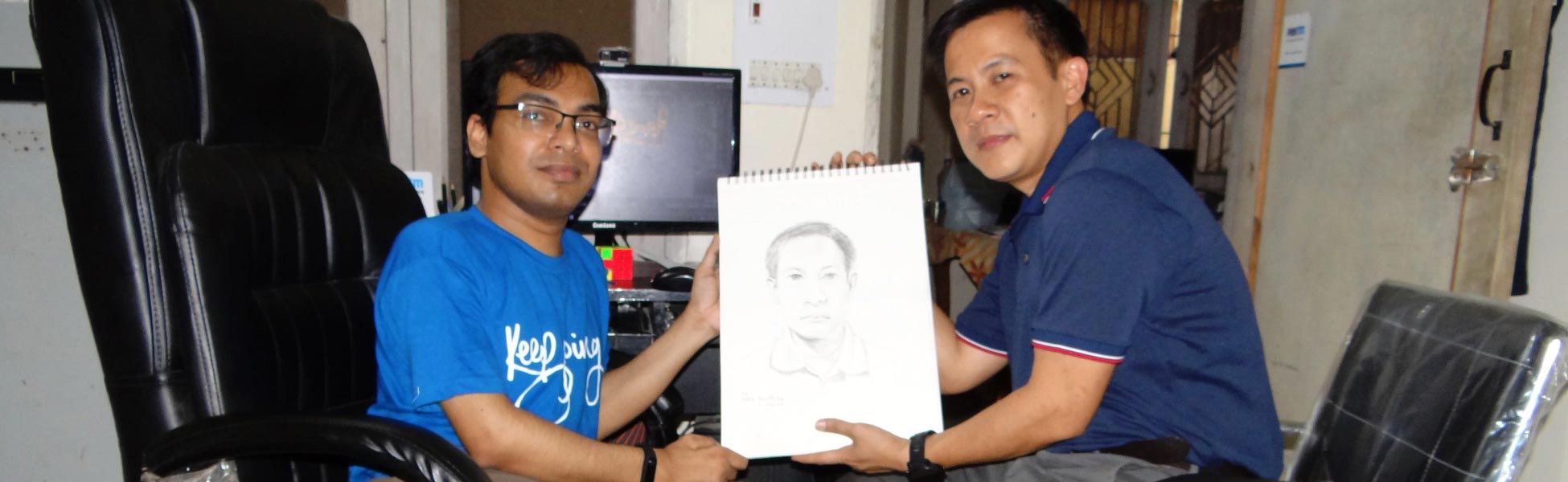 Artist Kamal Nishad smiling alongside a client in a studio while together holding a framed 1-minute hand-drawn pencil portrait sketch. fixer in Bhadrak, film fixer in Bhadrak, media fixer in Bhadrak, movie fixer in Bhadrak, production fixer in Bhadrak, line producer in Bhadrak
