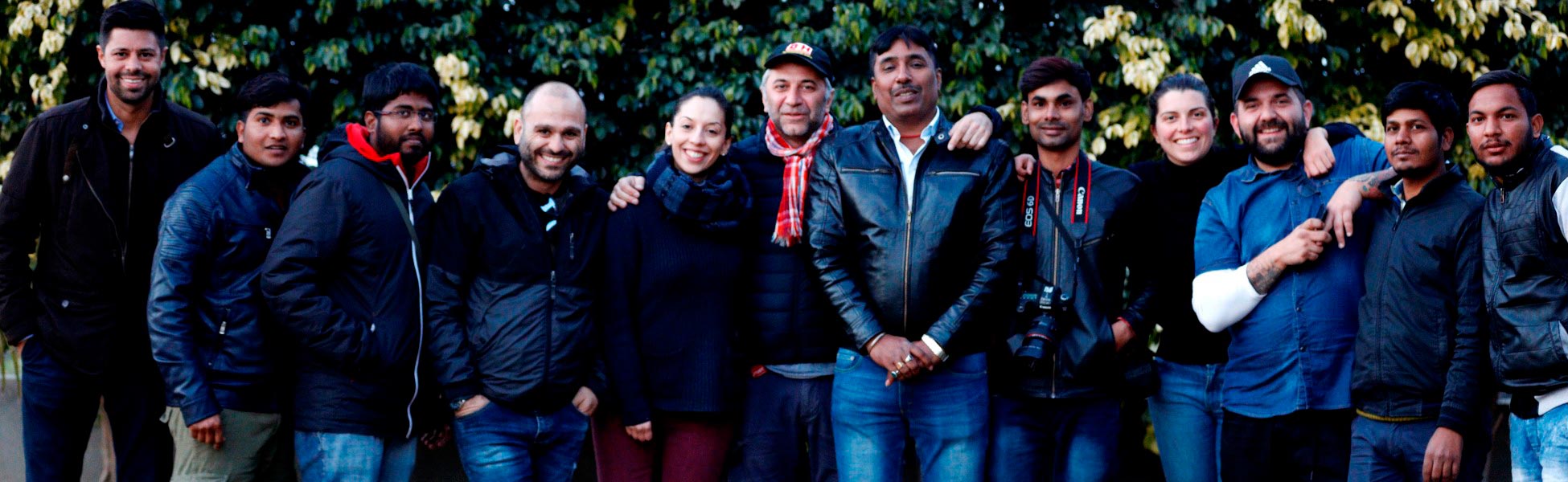 Group portrait of the diverse international film crew from Trisna Films®, the US, and Italy. The crew members are smiling and posing together outdoors in front of a leafy green background while on location in Ludhiana, Punjab, India, for the production of the web series 'All in The Family - Under One Roof'. film shooting locations in india, film shooting locations in Delhi, film shooting locations in mumbai, film shooting locations in pune, film shooting locations in sonipat, film shooting locations in begusarai, video shooting locations in india, video shooting locations in Delhi, video shooting locations in mumbai, video shooting locations in pune, video shooting locations in sonipat, video shooting locations in begusarai, tv shooting locations in india, tv shooting locations in delhi, tv shooting locations in mumbai, tv shooting locations in pune, tv shooting locations in sonipat, tv shooting locations in begusarai, shooting locations in india, shooting locations in delhi, shooting locations in mumbai, shooting locations in pune, shooting locations in sonipat, shooting locations in begusarai