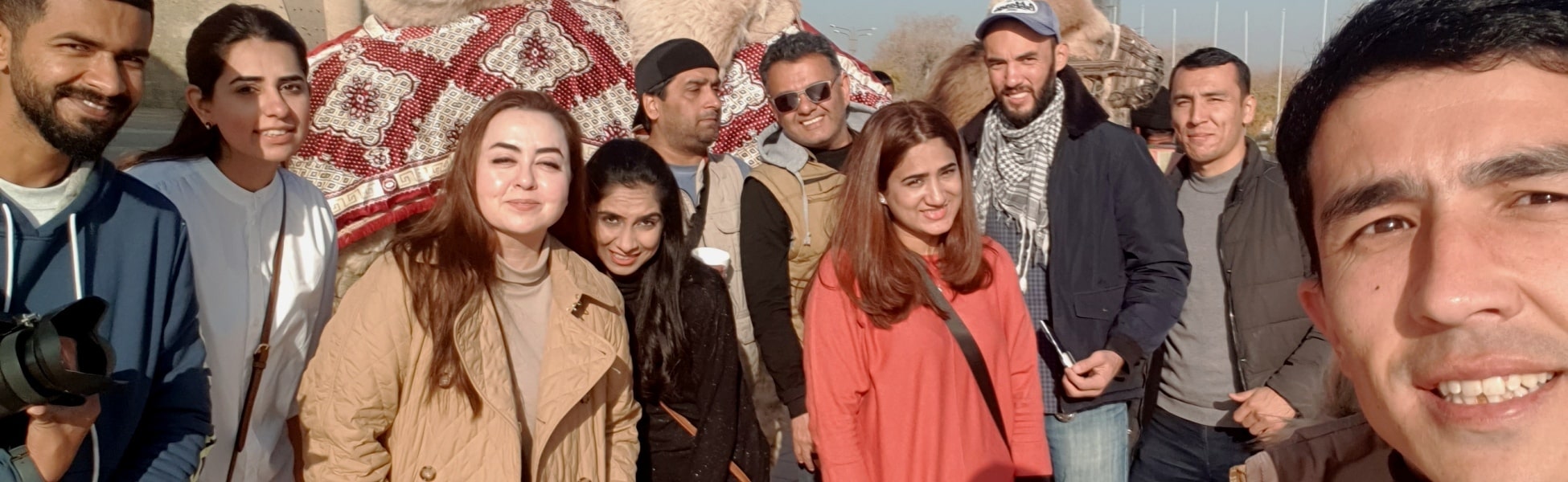 The Trisna Films® crew and the Maria.B. team taking a group selfie with decorated camels at the ancient Ark of Bukhara fortress in Uzbekistan during a professional fashion ad production. filmmaking workshop in india, filmmaking workshop in delhi, filmmaking workshop in mumbai, filmmaking workshop in pune, filmmaking workshop in sonipat, filmmaking workshop in begusarai, cinematography workshop in india, cinematography workshop in delhi, cinematography workshop in mumbai, cinematography workshop in pune, cinematography workshop in sonipat, cinematography workshop in begusarai, camera workshop in india, camera workshop in delhi, camera workshop in mumbai, camera workshop in pune, camera workshop in sonipat, camera workshop in begusarai, editing workshop in india, editing workshop in delhi, editing workshop in mumbai, editing workshop in pune, editing workshop in sonipat, editing workshop in begusarai, vfx workshop in india, vfx workshop in Delhi, vfx workshop in mumbai, vfx workshop in pune, vfx workshop in sonipat, vfx workshop in begusarai, animation workshop in india, animation workshop in Delhi, animation workshop in mumbai, animation workshop in pune, animation workshop in sonipat, animation workshop in begusarai, photography workshop in india, photography workshop in delhi, photography workshop in mumbai, photography workshop in pune, photography workshop in sonipat, photography workshop in begusarai, direction workshop in india, direction workshop in delhi, direction workshop in mumbai, direction workshop in pune, direction workshop in sonipat, direction workshop in begusarai, script writing workshop in india, script writing workshop in delhi, script writing workshop in mumbai, script writing workshop in pune, script writing workshop in sonipat, script writing workshop in begusarai