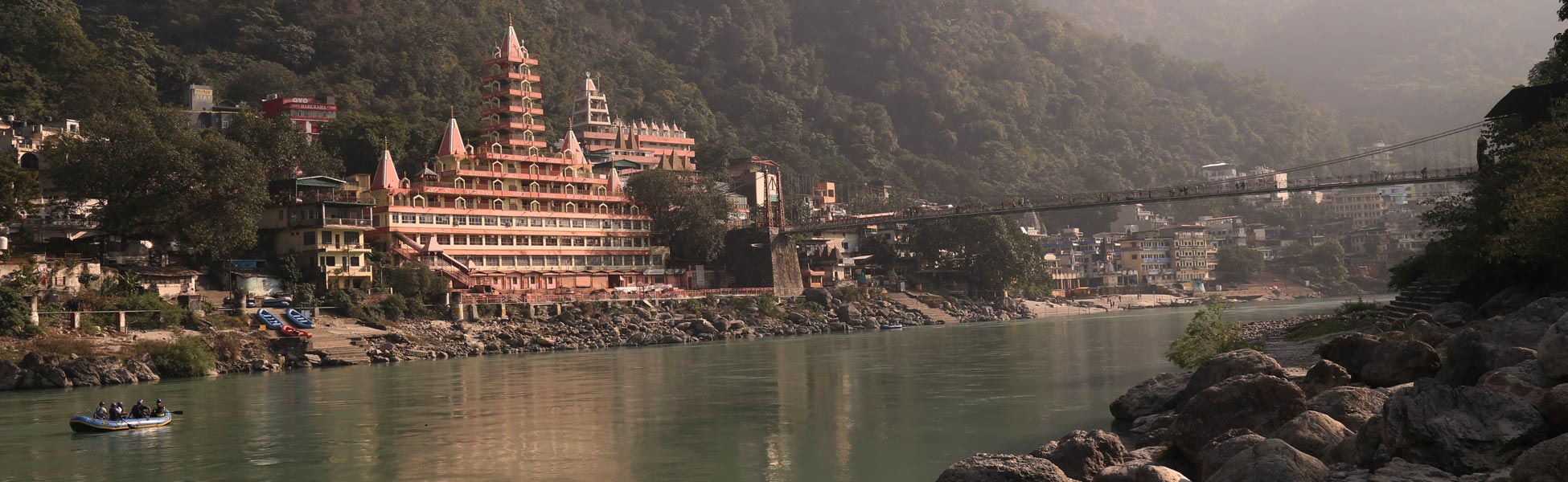 Scenic film shooting location along the holy River Ganges in Rishikesh, Uttarakhand, featuring the iconic Tera Manzil Temple and a suspension bridge against a lush mountainous backdrop. film production house in Anupgarh, video production house in Anupgarh, tv production house in Anupgarh, production house in Anupgarh, film production company in Anupgarh, video production company in Anupgarh, tv production company in Anupgarh, production company in Anupgarh