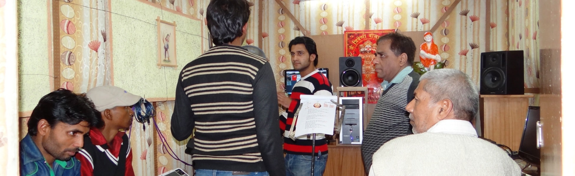 A group of music producers and artists collaborating inside a small digital audio recording studio in Delhi, featuring studio monitors, a computer screen running a DAW, and a lyric sheet stand. film shooting locations in Ballari, video shooting locations in Ballari, tv shooting locations in Ballari, shooting locations in Ballari