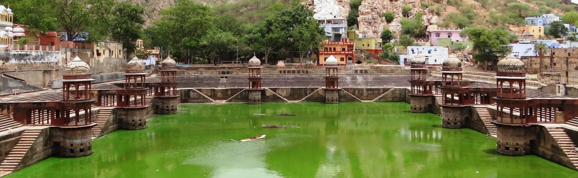 Panoramic wide shot of Sagar Kund step-pond in Alwar, Rajasthan, featuring symmetrical red sandstone chhatris (cenotaphs) along the emerald green water, situated below the Aravalli hills and adjacent to Moosi Maharani ki Chhatri. fixer in Ballari, film fixer in Ballari, media fixer in Ballari, movie fixer in Ballari, production fixer in Ballari, line producer in Ballari